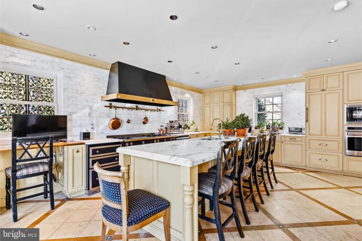 Kitchen showcases a large marble-topped island surrounded by bar seating and equipped with a deep sink.