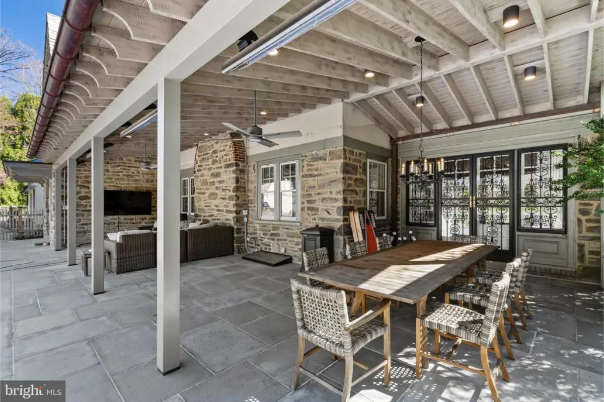 A spacious patio features stone walls and a wooden pergola-style roof with recessed lighting and ceiling fans.