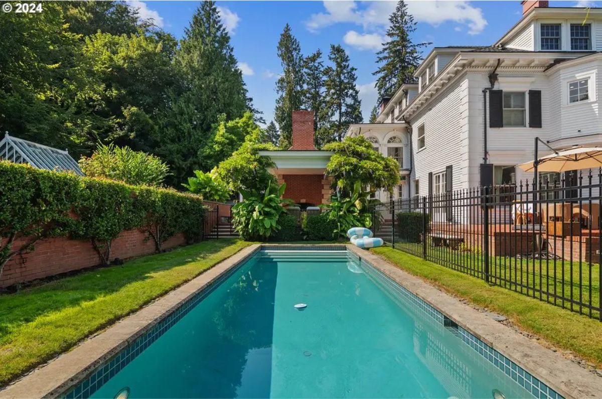 Rectangular swimming pool is surrounded by lush greenery and a red brick wall for privacy.