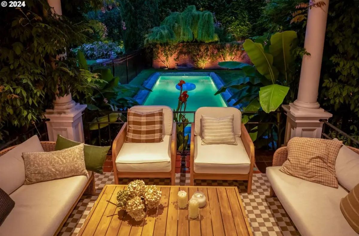 Cozy seating area overlooks a rectangular swimming pool surrounded by lush greenery.