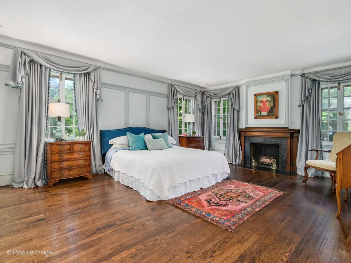 Spacious bedroom features a blue upholstered bed with matching pillows, adding a pop of color to the soft palette.