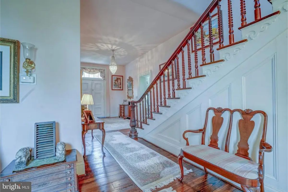 Entryway featuring a polished wooden staircase with intricate spindles and a paneled wall.