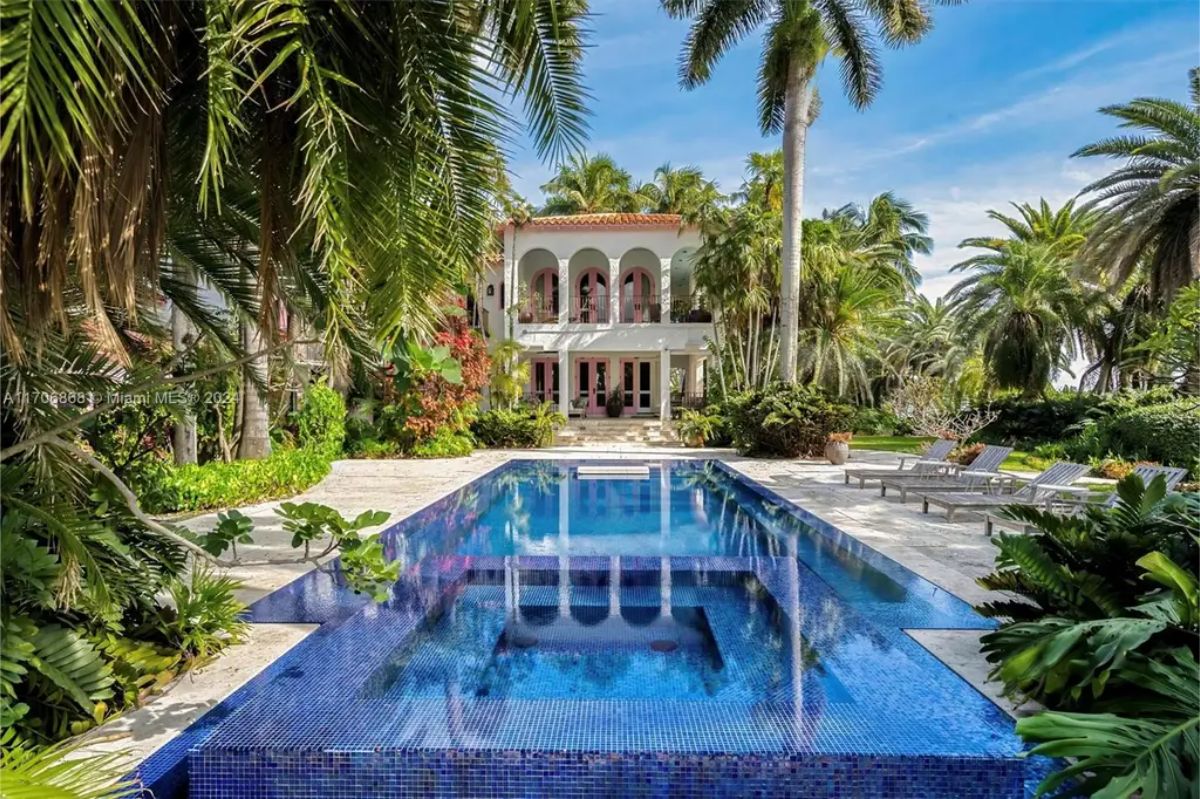 Elegant villa surrounded by lush tropical landscaping, showcasing a vibrant blue mosaic pool with integrated spa.