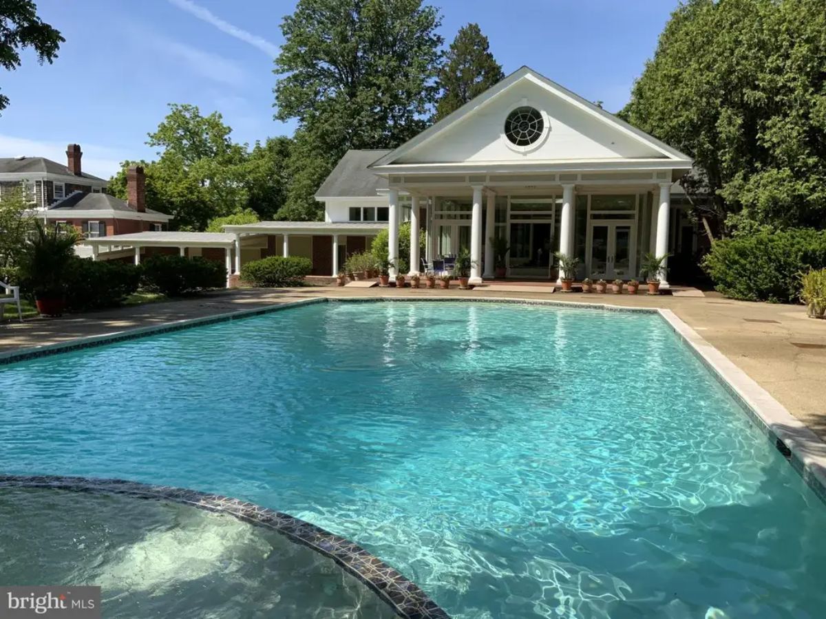 Expansive outdoor pool adjacent to a pavilion-style building with large columns and symmetrical design.