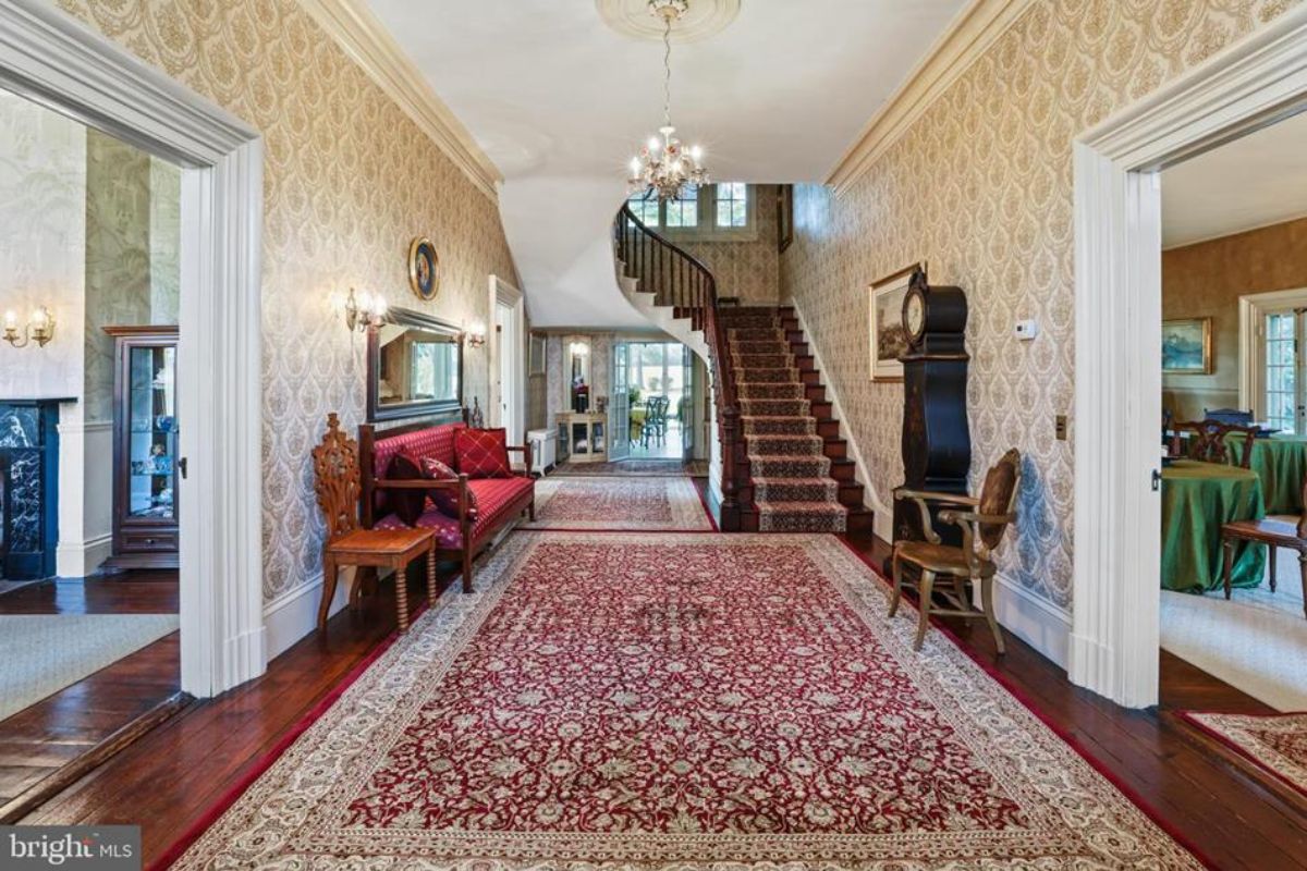 Entry hall featuring patterned wallpaper, polished hardwood floors, and a red carpet runner.