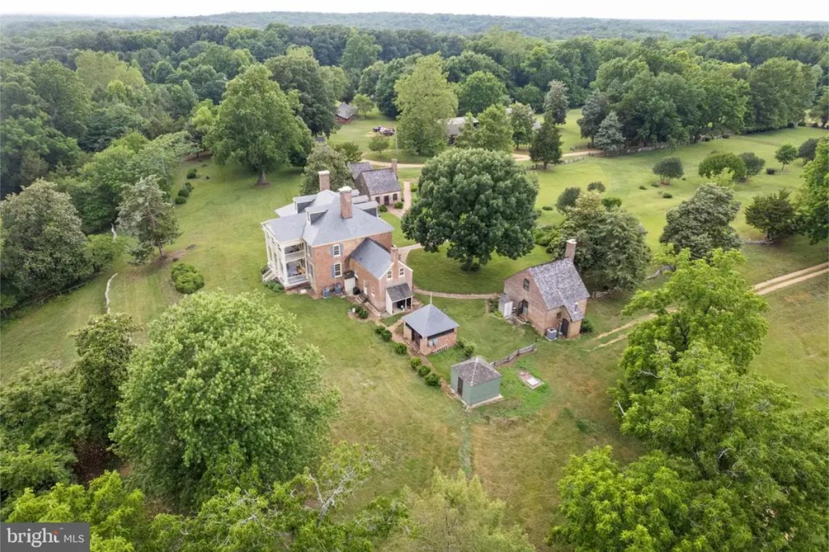 This aerial view highlights the property's expansive grounds surrounded by lush greenery and mature trees.