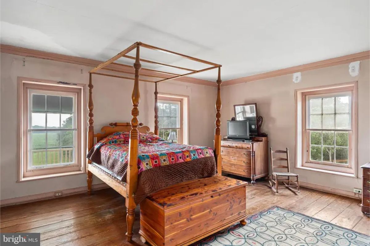 The room features a four-poster bed as the central piece, complemented by wooden floors and rustic furniture.