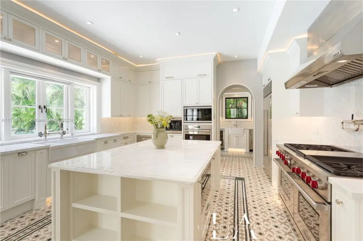 Spacious white kitchen with custom cabinetry, marble countertops, and a central island with open shelving.