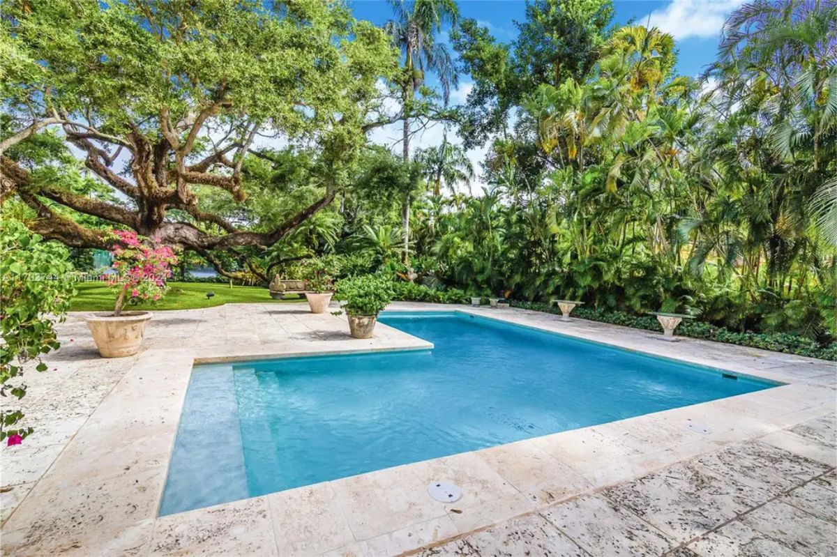 Expansive pool area surrounded by lush tropical greenery and mature trees providing shade and privacy.