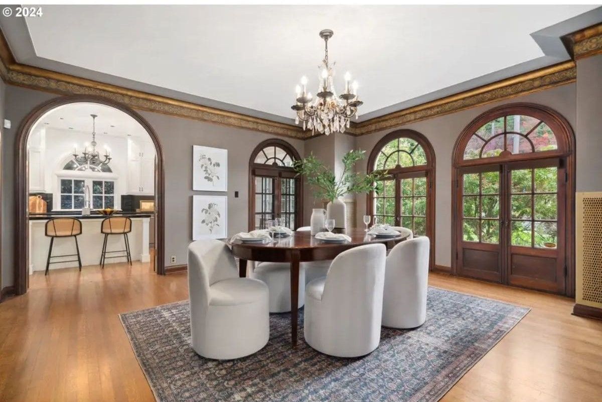 Round wooden table surrounded by white upholstered chairs on a patterned area rug.