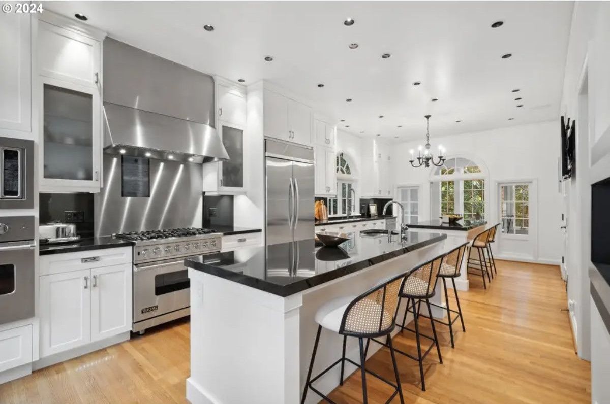 Kitchen features white cabinetry, black countertops, and a large stainless steel range with a matching hood.