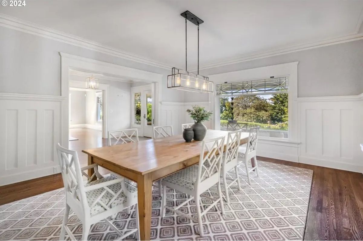 A wooden table and eight white chairs placed on a geometric-patterned rug.