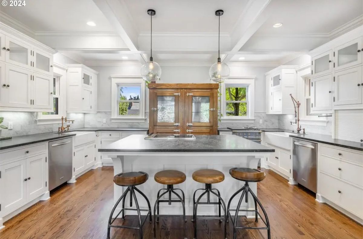 A white kitchen with shaker-style cabinets, marble countertops, and hardwood flooring.