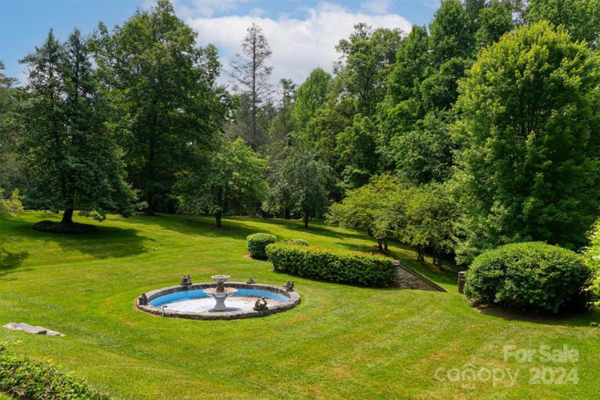 Landscape showcases a round fountain bordered by stonework on a well-maintained grassy lawn.