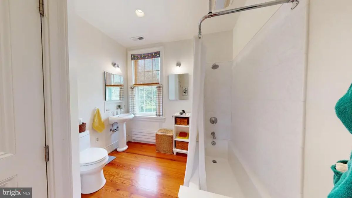 Bathroom features a clean, minimalist design with a white pedestal sink and a full bathtub with a shower.