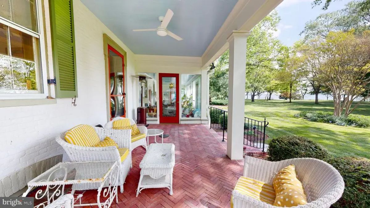 Covered porch overlooks a lush, expansive lawn with scenic views of surrounding greenery.