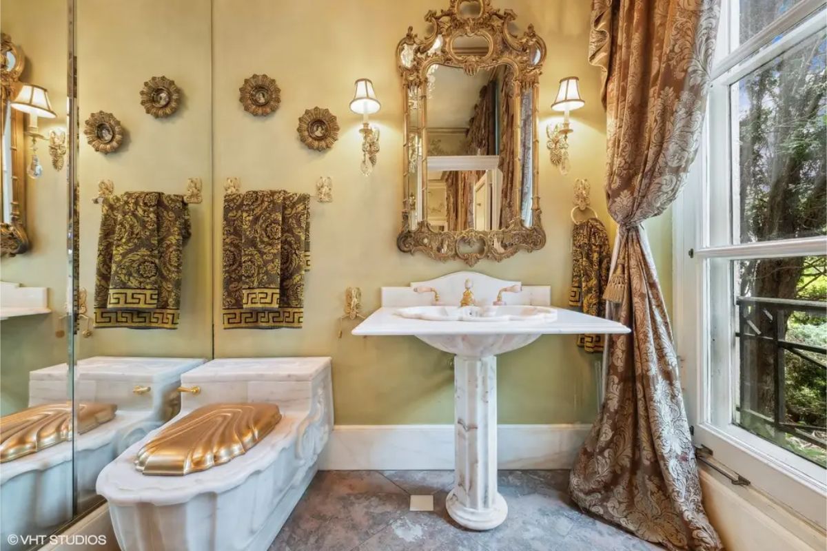 Pedestal sink and intricately carved mirror enhance the room's opulent design.