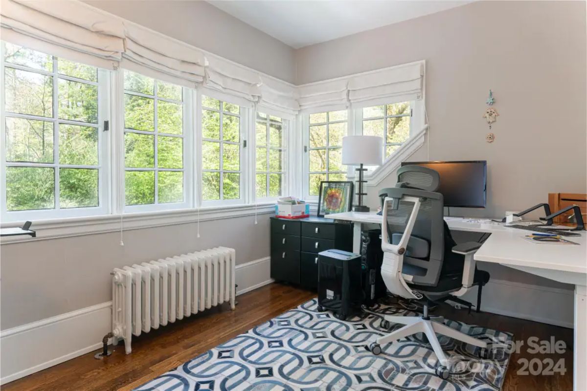 Home office is bathed in Natural light from corner windows with Roman shades, offering serene outdoor views.