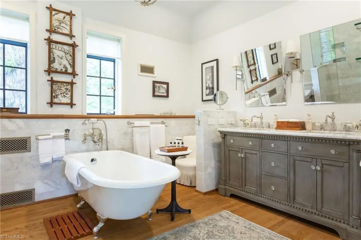 A clawfoot bathtub with vintage-style fixtures against a marble-tiled wall.