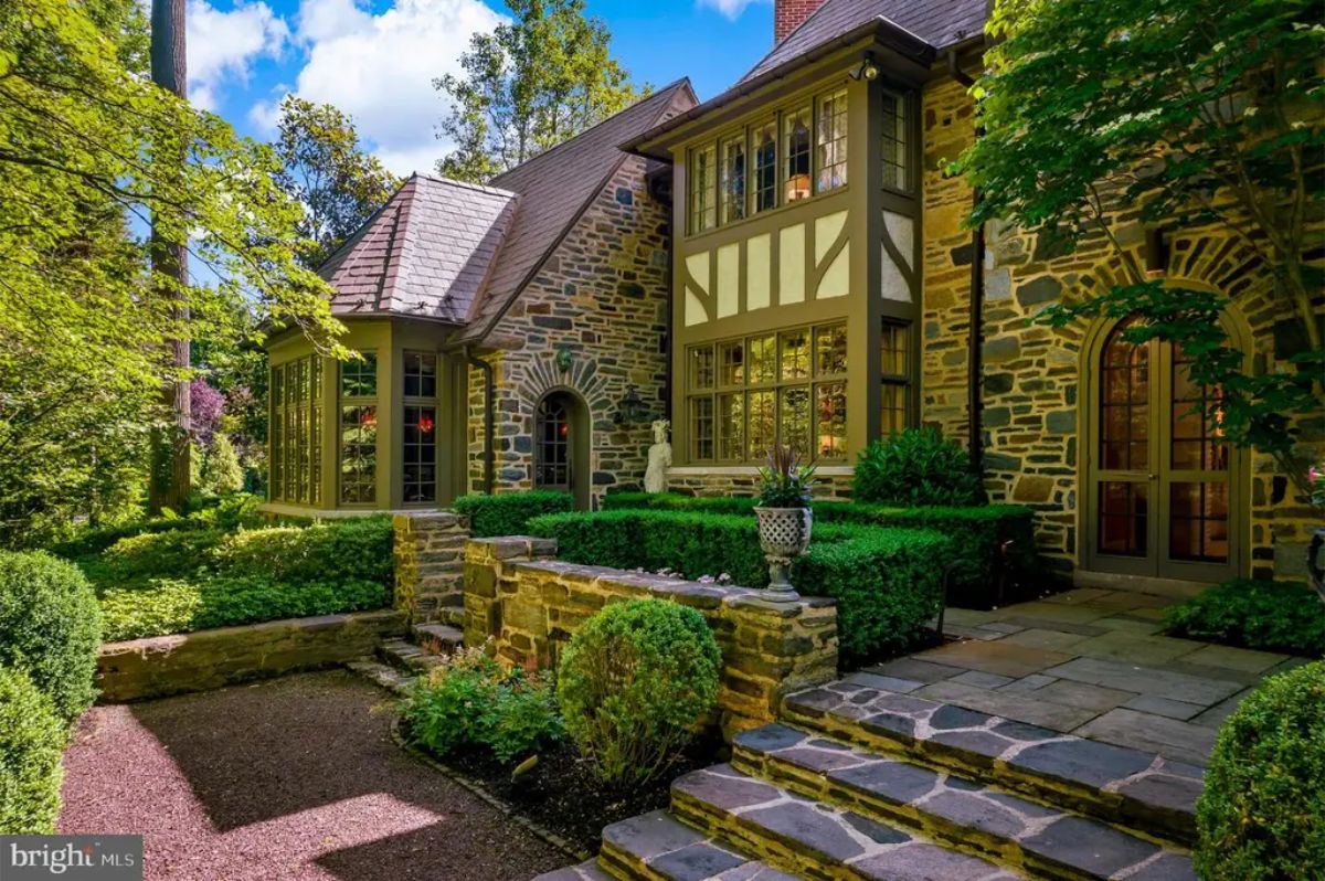 Built with classic Tudor architectural details, the residence showcases a stone façade with steeply pitched gables and elegant leaded windows.