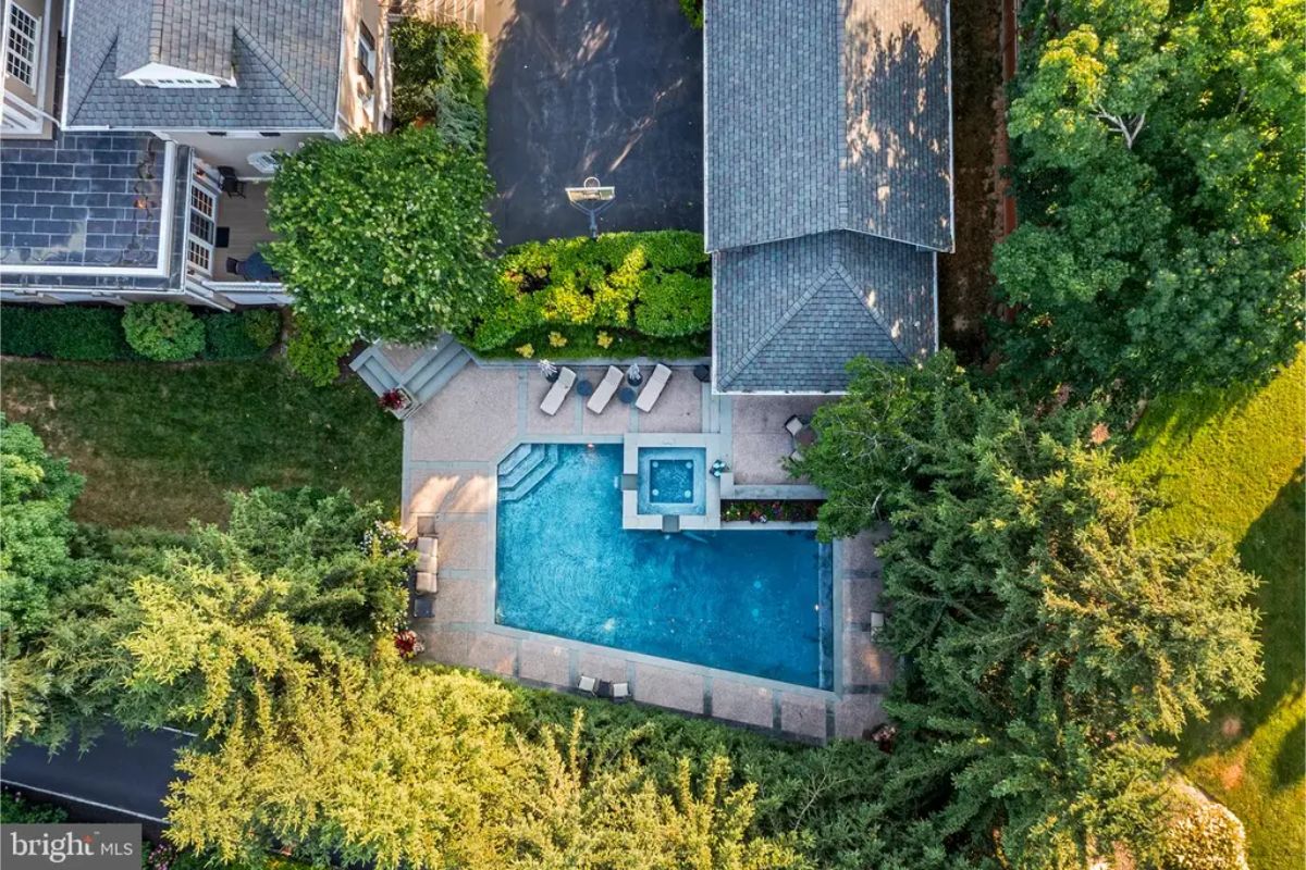 Rectangular pool with attached hot tub sits centrally within a landscaped backyard.