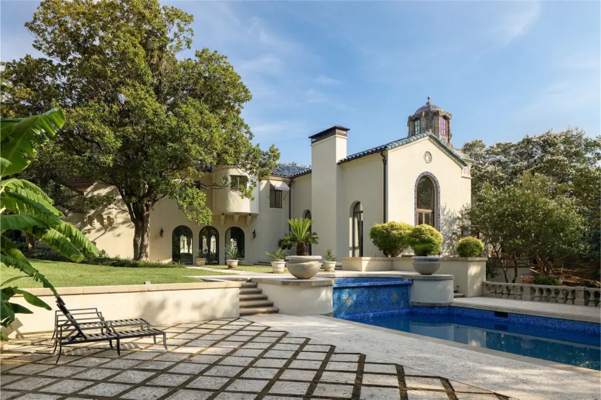 Mediterranean-style home surrounded by lush greenery, showcasing arched windows and a tile roof.