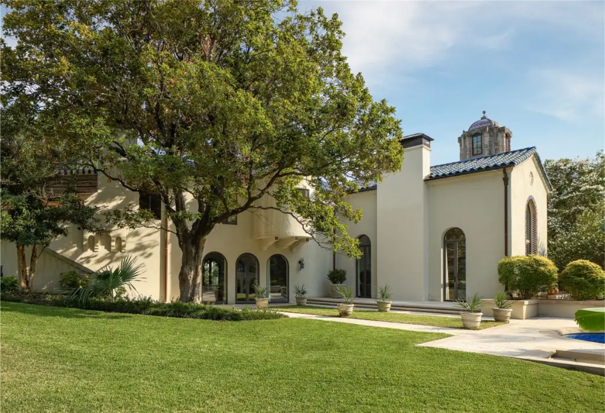 Stucco-clad Mediterranean residence framed by mature trees and lush greenery.