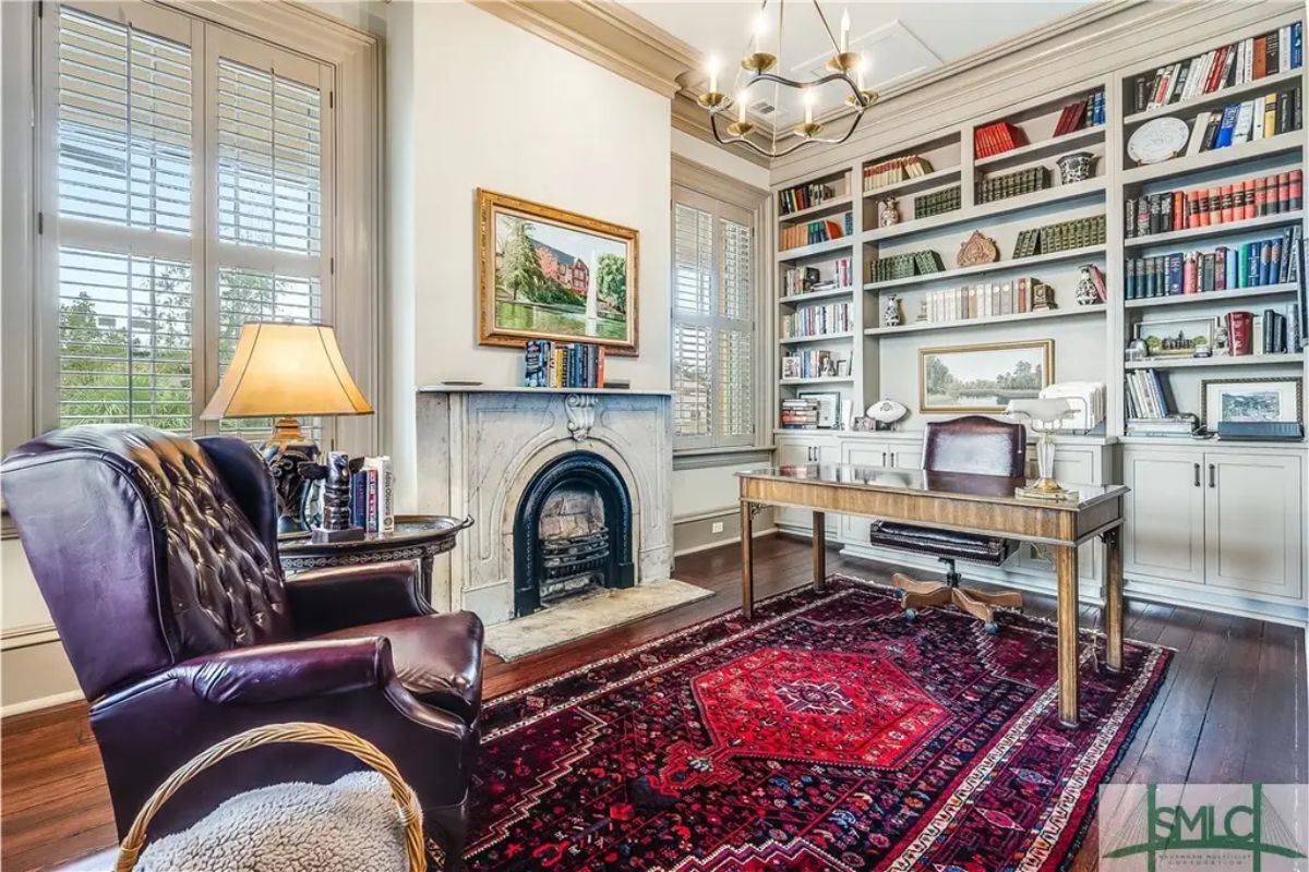 A home office showcases built-in shelves filled with books and decorative items, flanking a classic white fireplace.