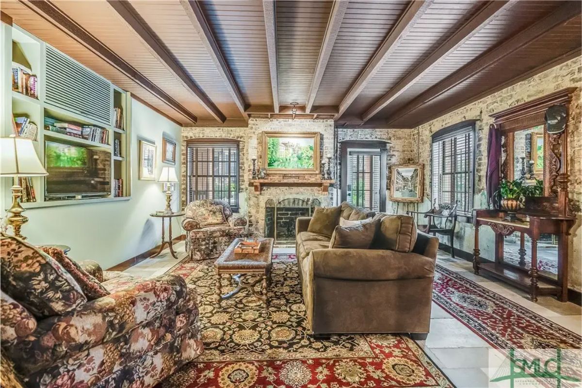 Exposed brick walls surround the cozy living room, complemented by a beamed ceiling.