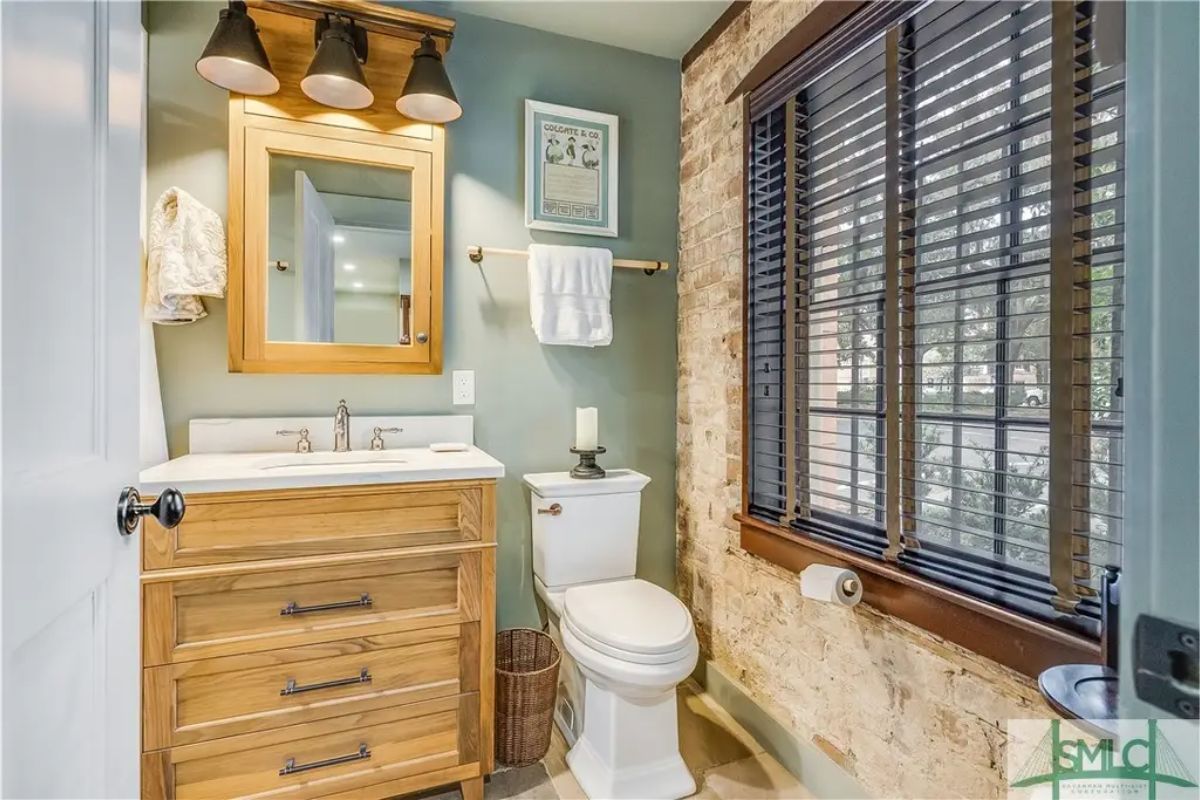 Small bathroom with a rustic brick accent wall and muted green painted walls.