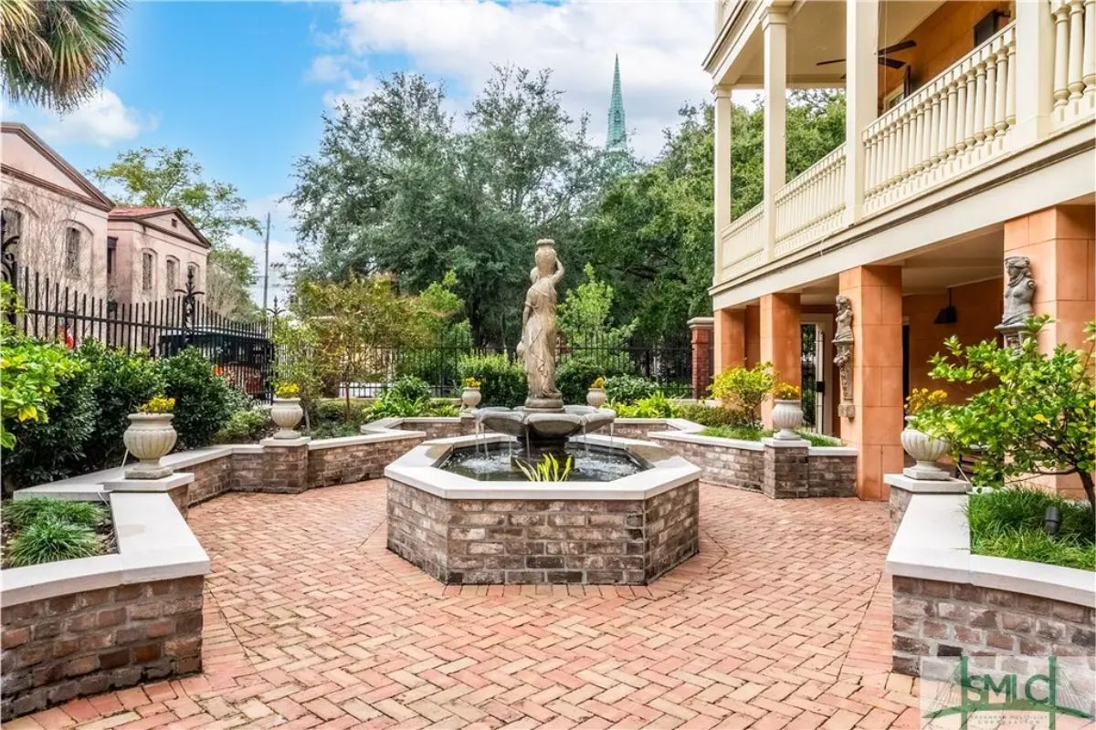 Brick courtyard centered around a multi-tiered fountain with a classical statue.