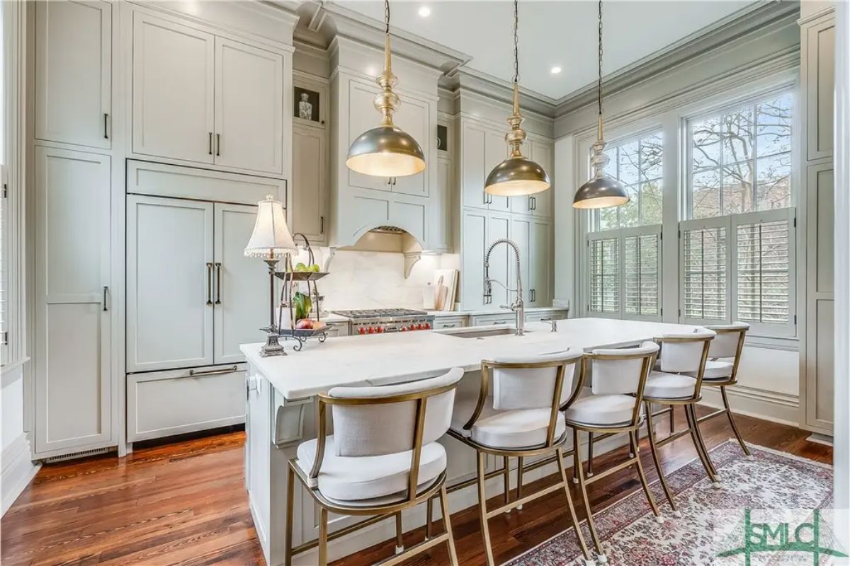 Large white marble island with seating for six, accented by gold-framed chairs.