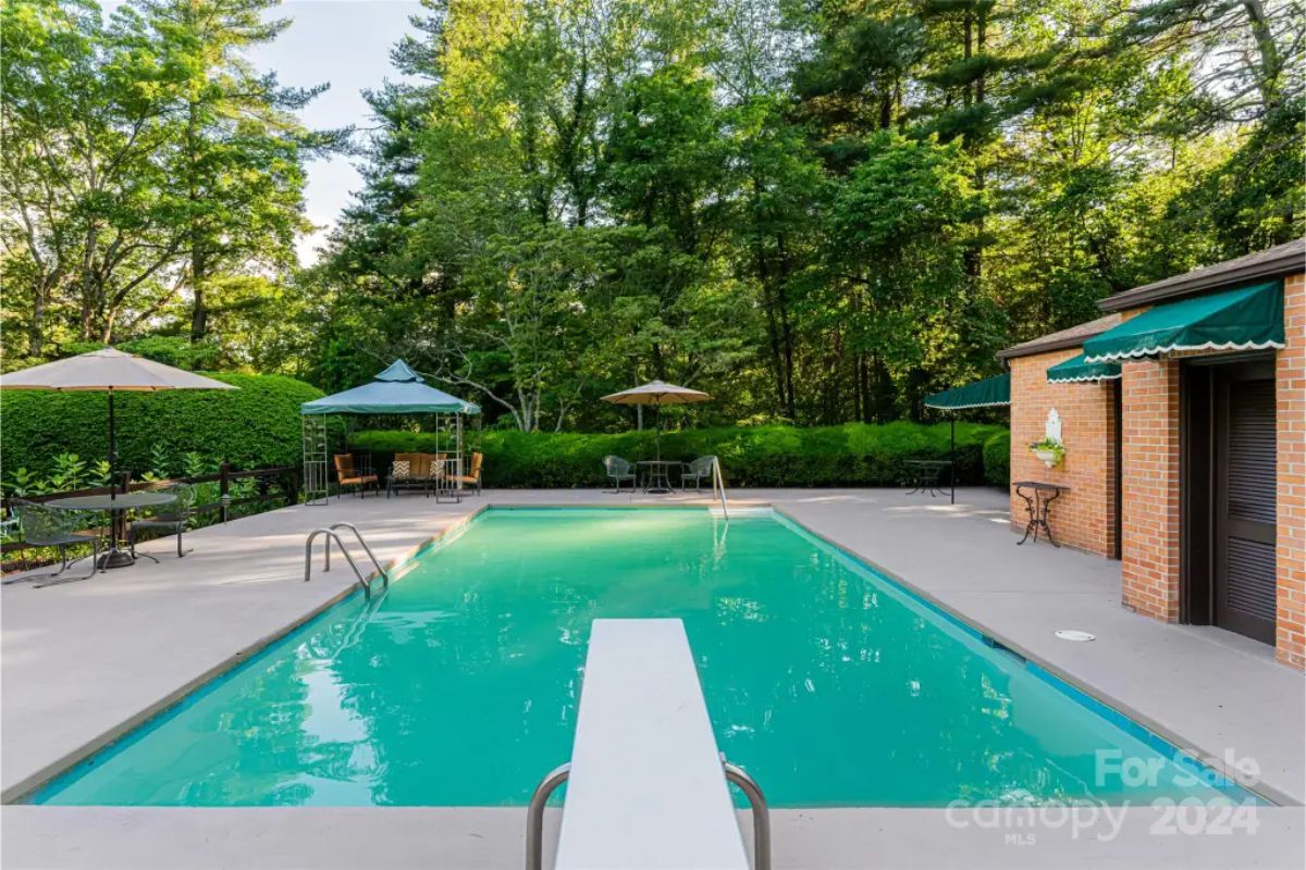 Pool is surrounded by a spacious concrete deck with seating and shaded areas under umbrellas and a gazebo.