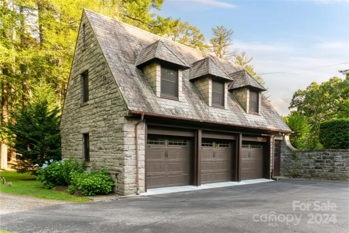 Garage structure features stone construction with a steep slate roof and three dormer windows.