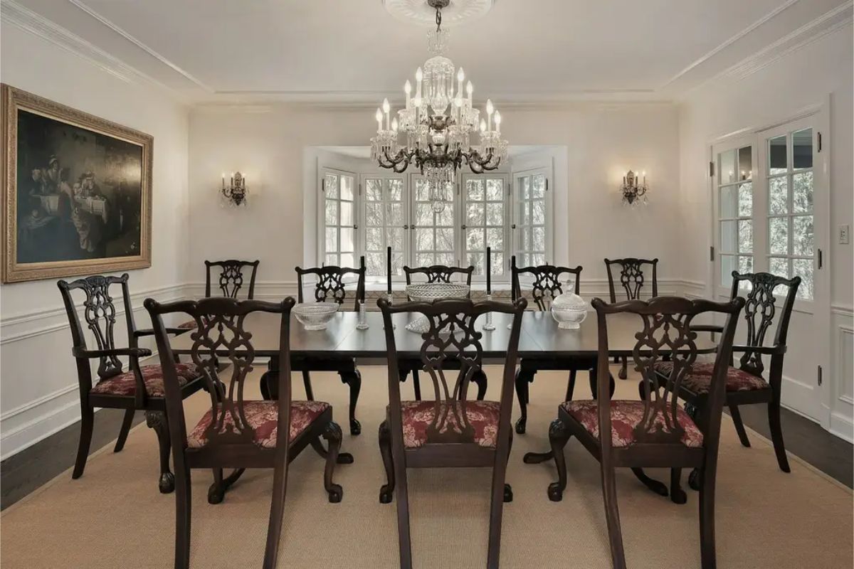 Crystal chandelier serves as the centerpiece, casting light over a dark wood dining table and intricately carved chairs.