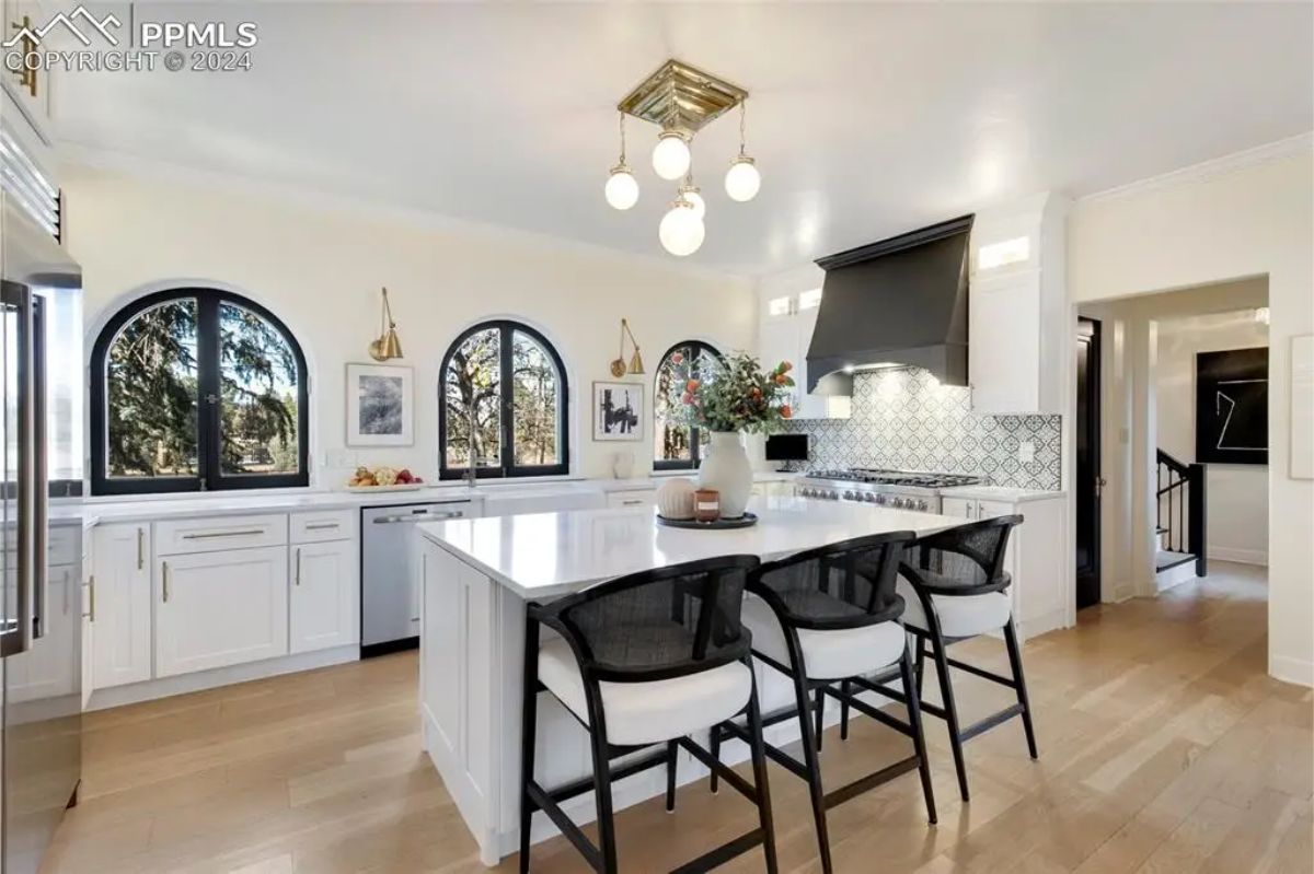 Sleek white cabinetry, a spacious central island with seating, and contemporary lighting fixtures. 