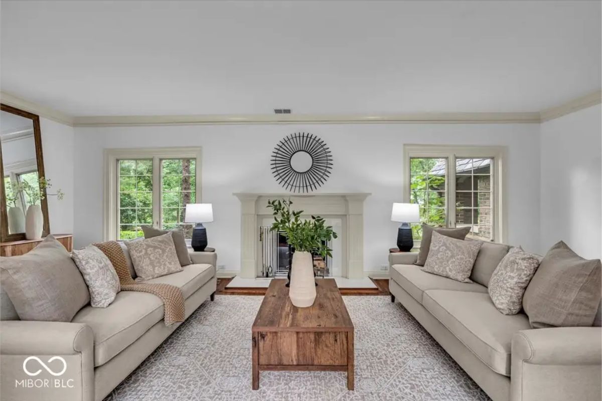 A spacious living room features neutral-toned sofas arranged around a rustic wooden coffee table. 