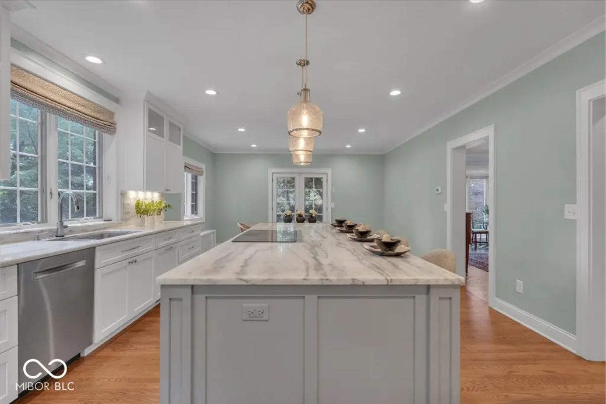 The kitchen features a long marble-topped island with seating for casual dining and pendant lighting above.