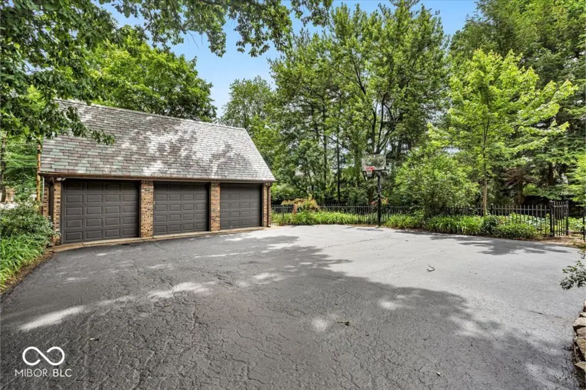 Detached three-car garage with classic brick construction and a slate roof is set amid lush greenery.