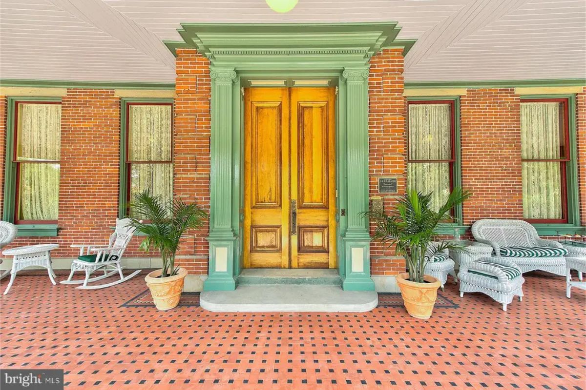 The front porch of Baywood Mansion showcases Victorian elegance with its detailed wood double doors and ornate green trim.