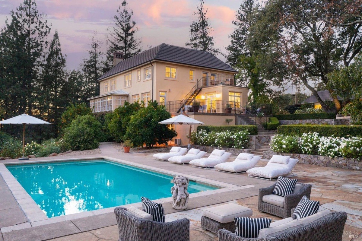 Large house has a swimming pool, patio furniture, and landscaping at dusk.