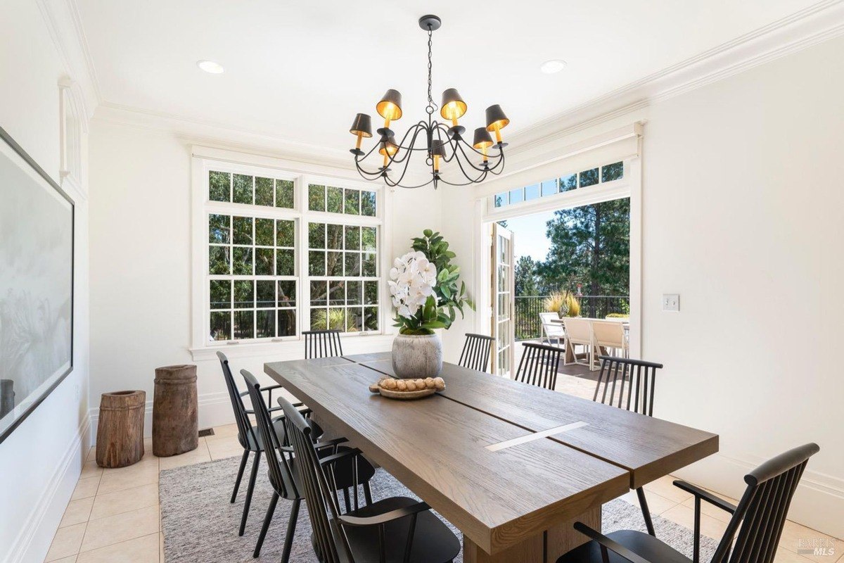 Dining room has a long wooden table with black chairs, a chandelier, and access to a patio with a view.