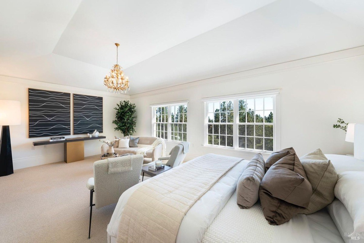 Master bedroom with a large bed, sitting area, and windows.