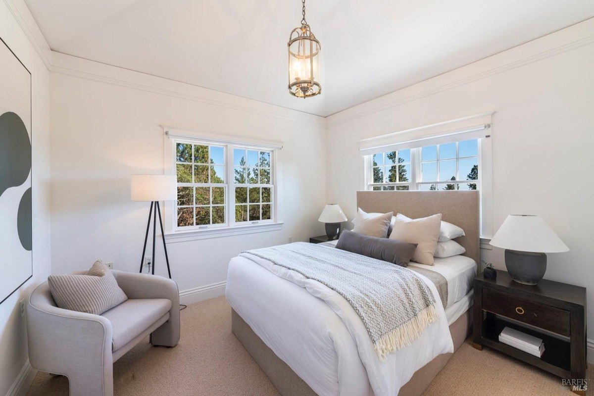 Guest bedroom has a sofa, a floor lamp, and windows with a view of trees.