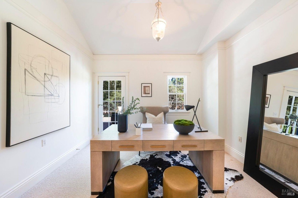 Office room with a large desk, comfortable seating, and natural light streaming in.