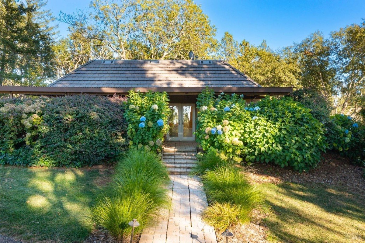 Ranch-style house with a stone walkway leading to a front entrance flanked by colorful hydrangea bushes.