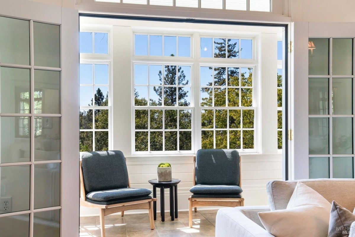 Sunroom has large windows, two armchairs, and a view of trees.