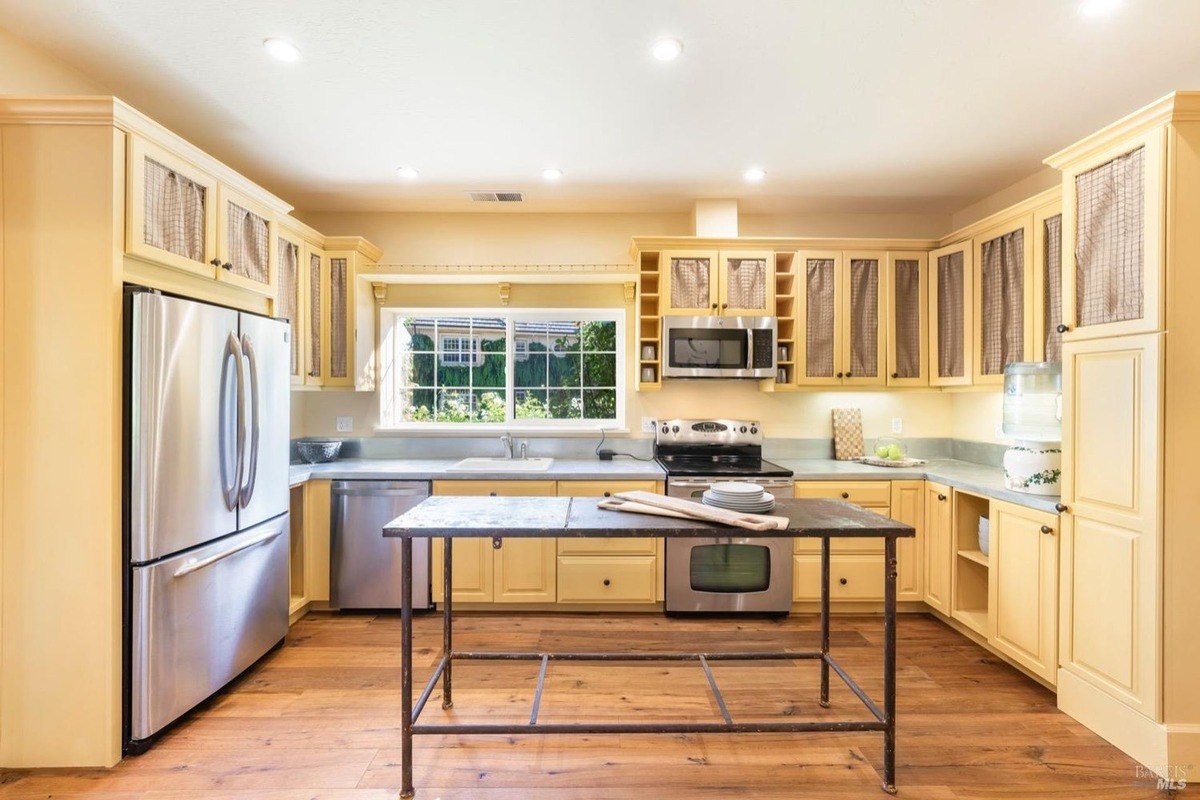 Kitchen has yellow cabinets, stainless steel appliances, and a large island in the center.