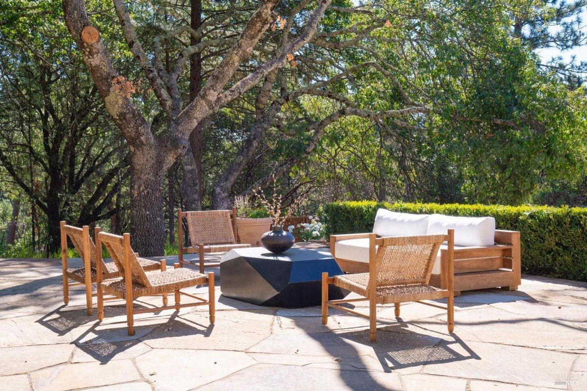 Patio furniture set includes a sofa, armchairs, and a geometric coffee table situated under trees.