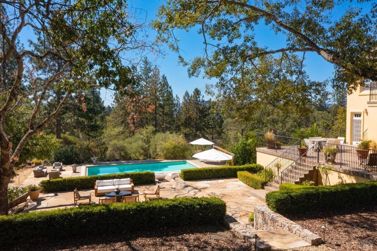 Pool area has patio furniture, landscaping, and a view of trees and hills.